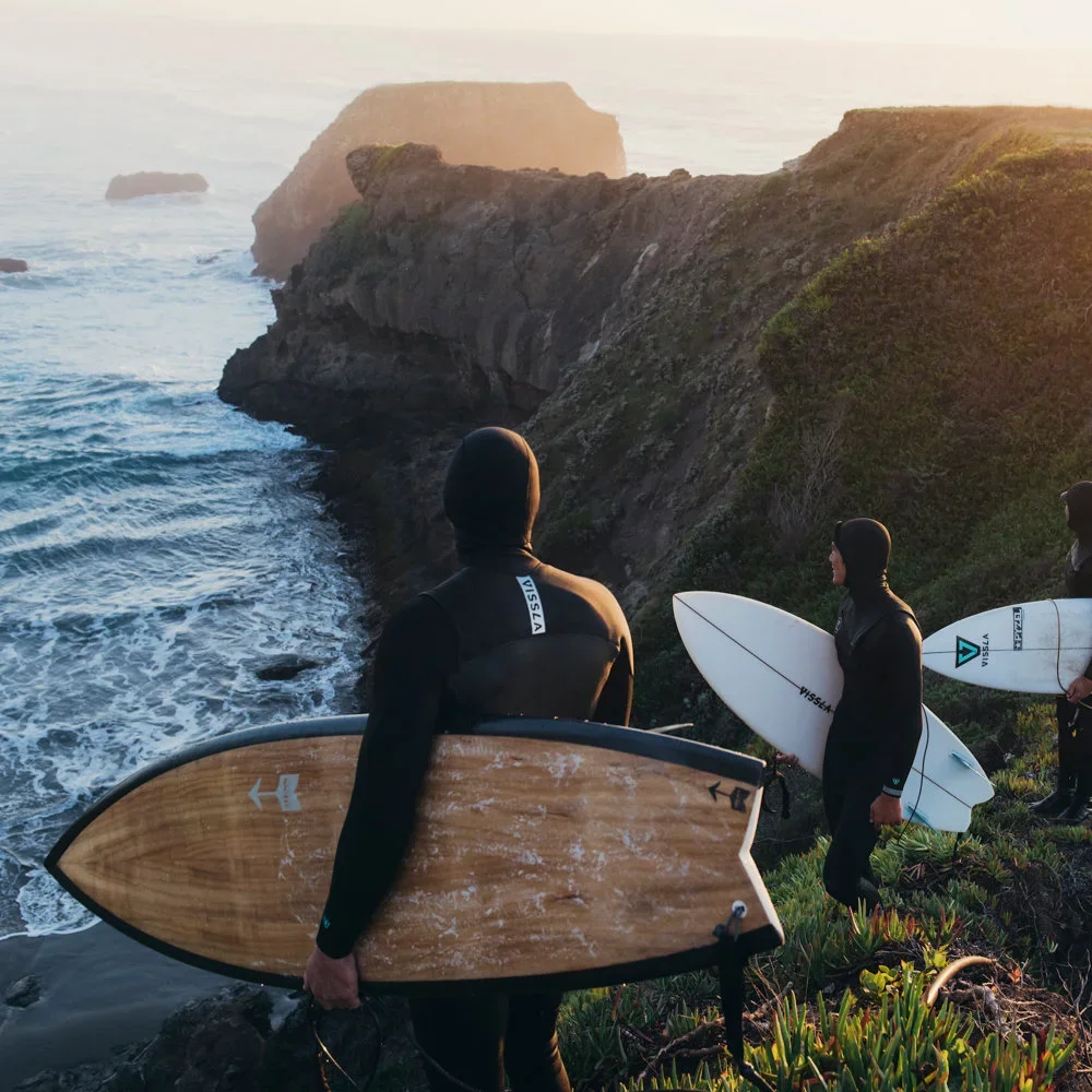 Surfeurs sur la falaise avec des planches de surf et des combinaisons à capuche de Vissla